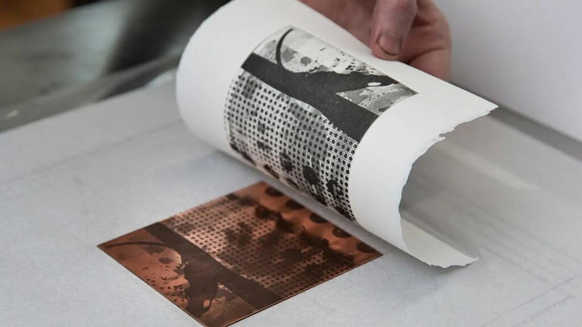 Gambar yang menunjukkan proses cetak ukiran, menampilkan seorang seniman yang mengukir permukaan papan kayu dengan alat ukir. Tinta kemudian dioleskan pada permukaan, dan cetakan dibuat dengan menekan kertas pada papan. [Pengertian cetak dalam]